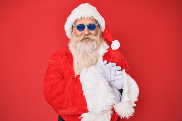 Old senior man wearing santa claus costume and sunglasses smiling with hands on chest with closed eyes and grateful gesture on face. health concept.