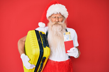 Old senior man wearing santa claus costume holding suicase and boarding pass skeptic and nervous, frowning upset because of problem. negative person.