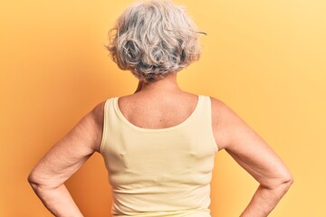 Senior grey-haired woman wearing casual clothes standing backwards looking away with arms on body