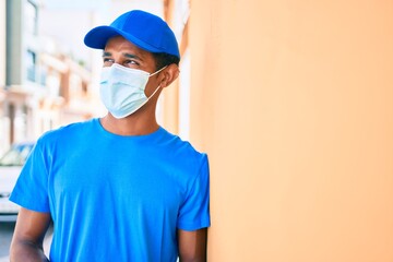 Fototapeta na wymiar African delivery man wearing courier uniform outdoors wearing coronavirus safety mask