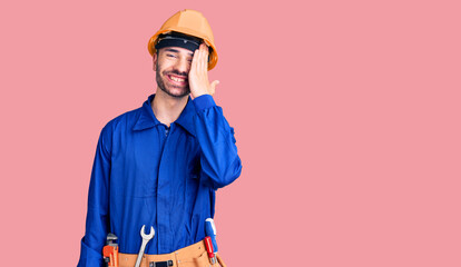 Young hispanic man wearing worker uniform covering one eye with hand, confident smile on face and surprise emotion.