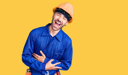 Young hispanic man wearing worker uniform smiling and laughing hard out loud because funny crazy joke with hands on body. - obrazy, fototapety, plakaty