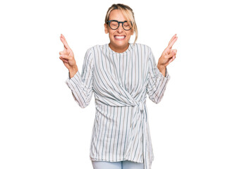 Beautiful blonde woman wearing business shirt and glasses gesturing finger crossed smiling with hope and eyes closed. luck and superstitious concept.