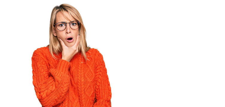 Beautiful blonde woman wearing casual clothes and glasses looking fascinated with disbelief, surprise and amazed expression with hands on chin
