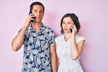 Beautiful couple having conversation talking on the smartphone thinking attitude and sober expression looking self confident