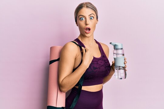 Beautiful blonde woman wearing sportswear holding water bottle and yoga mat afraid and shocked with surprise and amazed expression, fear and excited face.