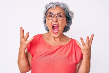 Senior hispanic grey- haired woman wearing casual clothes and glasses crazy and mad shouting and yelling with aggressive expression and arms raised. frustration concept.