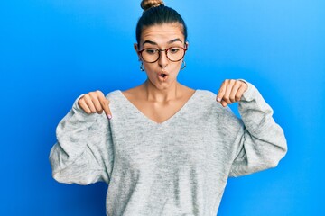 Young hispanic woman wearing casual clothes pointing down with fingers showing advertisement, surprised face and open mouth