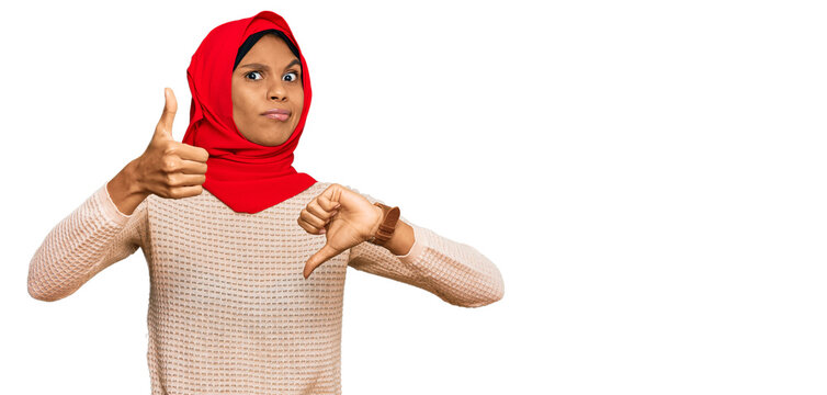Young african american woman wearing traditional islamic hijab scarf doing thumbs up and down, disagreement and agreement expression. crazy conflict