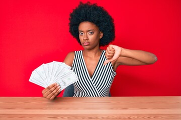 Young african american woman holding dollars with angry face, negative sign showing dislike with...