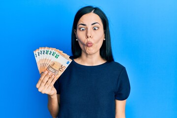 Beautiful young woman holding bunch of 50 euro banknotes making fish face with lips, crazy and comical gesture. funny expression.