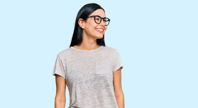 Beautiful young woman wearing casual clothes and glasses looking away to side with smile on face, natural expression. laughing confident.