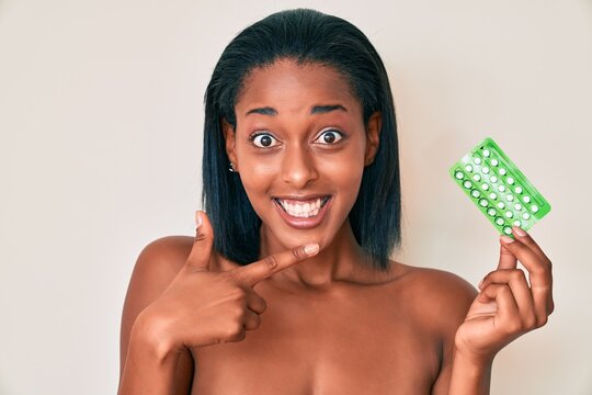 Young african american woman holding birth control pills smiling happy pointing with hand and finger