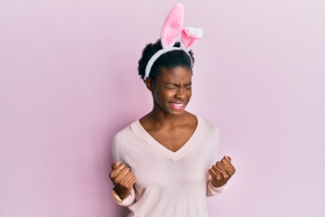 Young african american girl wearing cute easter bunny ears very happy and excited doing winner gesture with arms raised, smiling and screaming for success. celebration concept.
