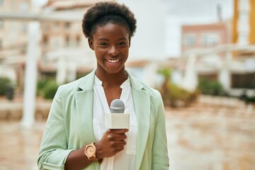 Young african american reporter woman using microphone at the city - obrazy, fototapety, plakaty