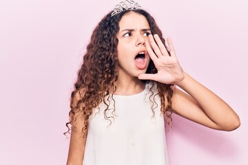 Beautiful kid girl with curly hair wearing princess tiara shouting and screaming loud to side with...