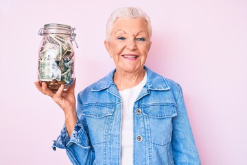 Senior beautiful woman with blue eyes and grey hair holding jar with savings looking positive and...