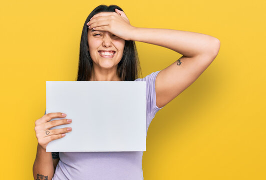Young hispanic woman holding blank empty banner stressed and frustrated with hand on head, surprised and angry face
