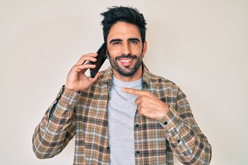 Handsome hispanic man with beard having conversation talking on the smartphone smiling with a happy...