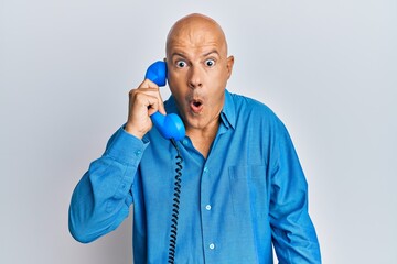 Middle age bald man speaking on vintage telephone scared and amazed with open mouth for surprise, disbelief face