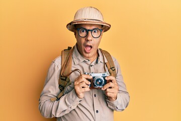 Middle age bald man wearing explorer hat and vintage camera afraid and shocked with surprise and...