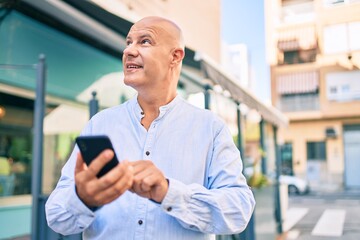 Fototapeta premium Middle age bald man smiling happy using smartphone at the city.