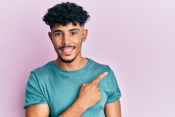 Young arab handsome man wearing casual clothes cheerful with a smile of face pointing with hand and finger up to the side with happy and natural expression on face