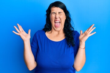 Plus size brunette woman wearing casual blue shirt celebrating mad and crazy for success with arms...