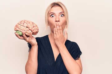 Young beautiful blonde woman asking for care memory holding brain over white background covering...