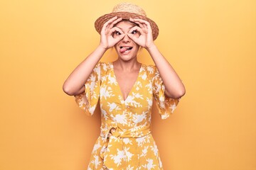 Beautiful blonde woman on vacation wearing summer hat and dress over yellow background doing ok...