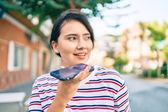 Young latin girl smiling happy sending voice message using smartphone at the city