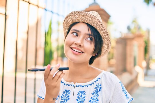 Young latin tourist girl on vacation smiling happy sending voice message using smartphone at the city.