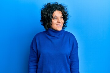 Fototapeta na wymiar Young hispanic woman with curly hair wearing casual winter sweater looking to side, relax profile pose with natural face and confident smile.