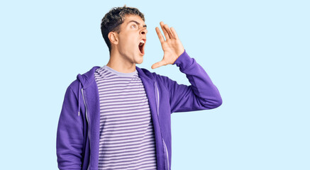 Young handsome man wearing casual purple sweatshirt shouting and screaming loud to side with hand on mouth. communication concept.