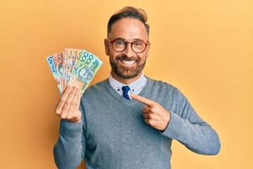 Handsome middle age man holding australian dollars smiling happy pointing with hand and finger