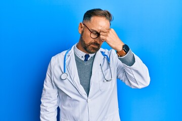 Handsome middle age man wearing doctor uniform and stethoscope tired rubbing nose and eyes feeling fatigue and headache. stress and frustration concept.