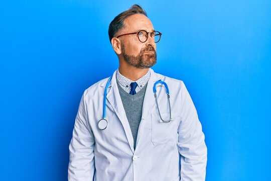 Handsome middle age man wearing doctor uniform and stethoscope smiling looking to the side and staring away thinking.