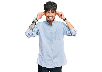 Young hispanic man wearing casual clothes smiling pulling ears with fingers, funny gesture....