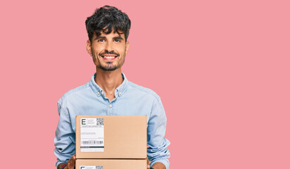 Young hispanic man holding delivery package looking positive and happy standing and smiling with a...