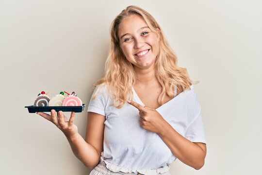 Young blonde girl holding cake sweets smiling happy pointing with hand and finger