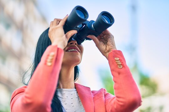 Young beautiful businesswoman smiling happy looking for new opportunities using binoculars at the city.