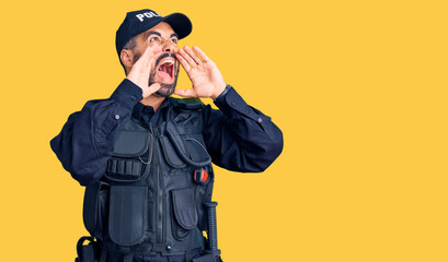 Young hispanic man wearing police uniform shouting angry out loud with hands over mouth