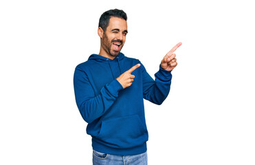 Young hispanic man wearing casual clothes smiling and looking at the camera pointing with two hands and fingers to the side.