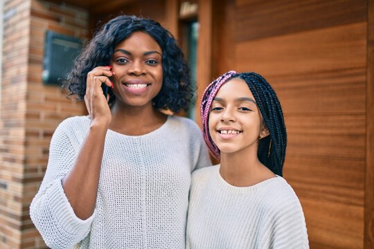 African american mother and daugther hugging and talking on the smartphone at the city.