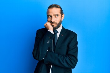 Attractive man with long hair and beard wearing business suit and tie thinking looking tired and bored with depression problems with crossed arms.