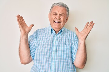Naklejka premium Senior grey-haired man wearing casual clothes celebrating mad and crazy for success with arms raised and closed eyes screaming excited. winner concept