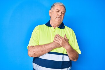 Senior grey-haired man wearing reflective t shirt smiling with hands on chest, eyes closed with...