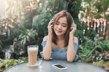 Young Asian woman sitting in café while using mobile phone and listening music outside.