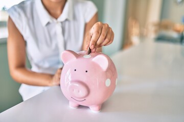 Young brunette woman smiling happy putting money savings inside of piggy bank