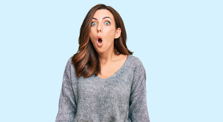 Young brunette woman wearing casual winter sweater scared and amazed with open mouth for surprise,...